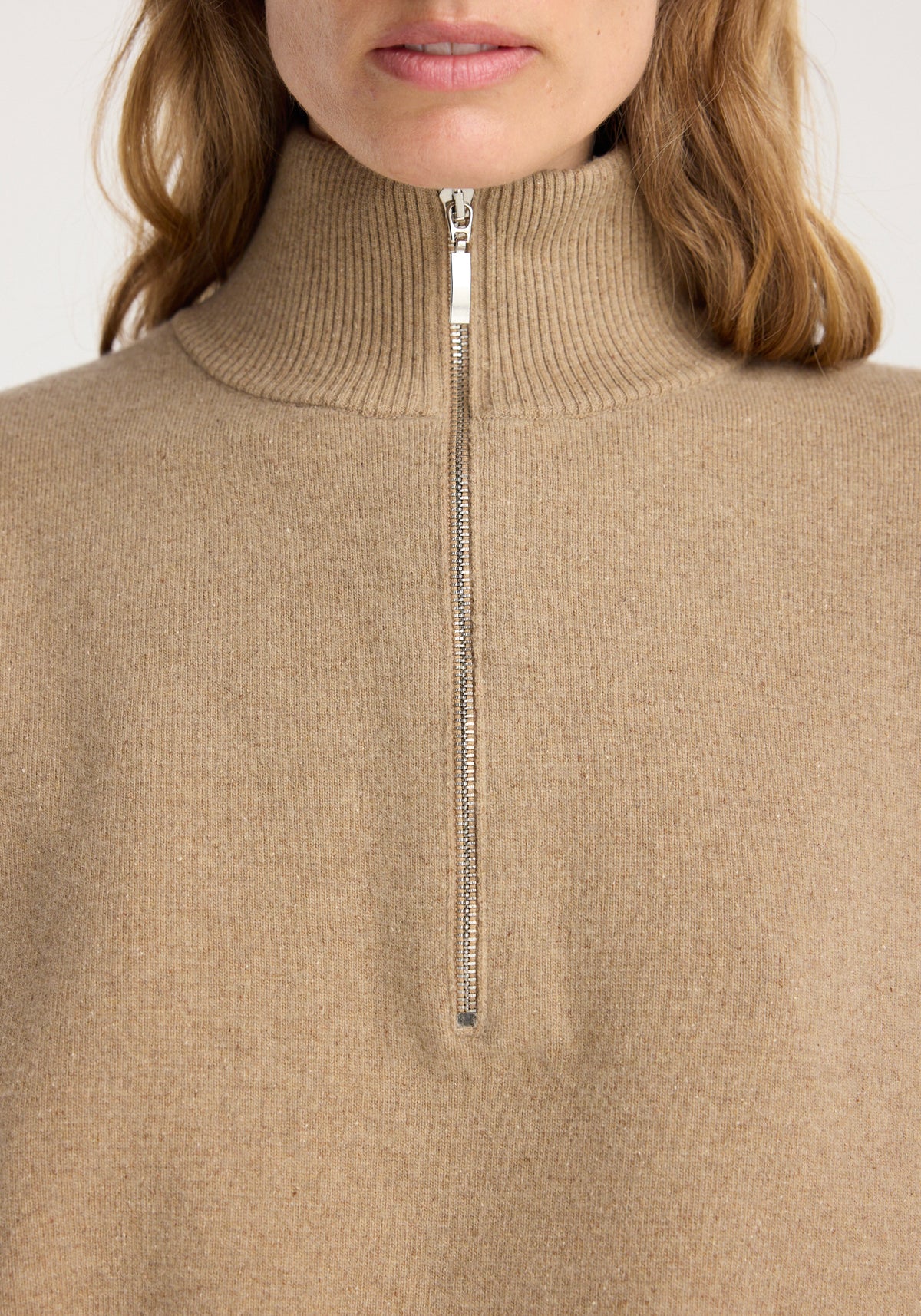 Close-up of a person wearing a zipped mouliné polo | camel with a high ribbed collar and silver zipper detail.