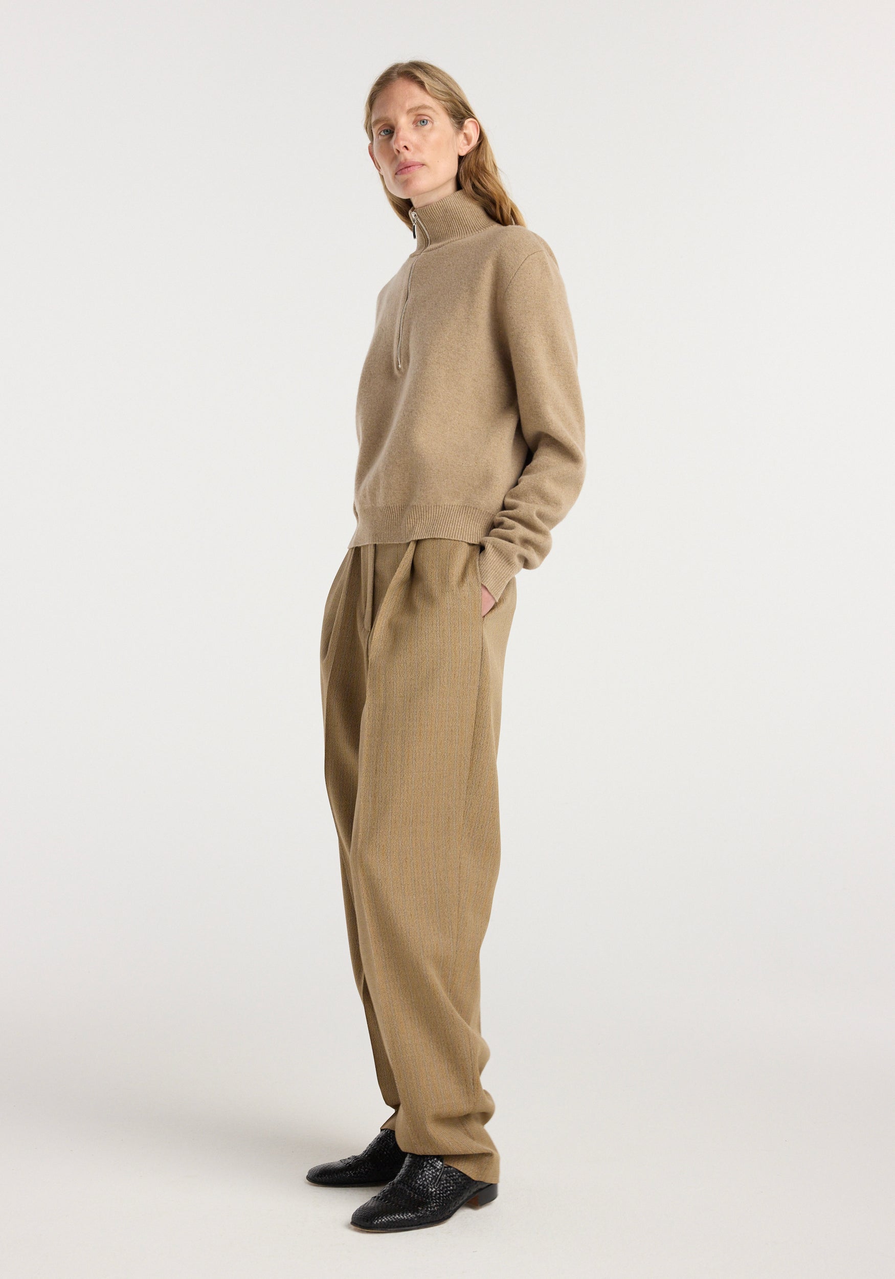 Woman wearing beige turtleneck sweater paired with Daria - Single pleat tapered trousers | heritage stripe in warm brown tones, styled with black textured shoes against a plain white background.