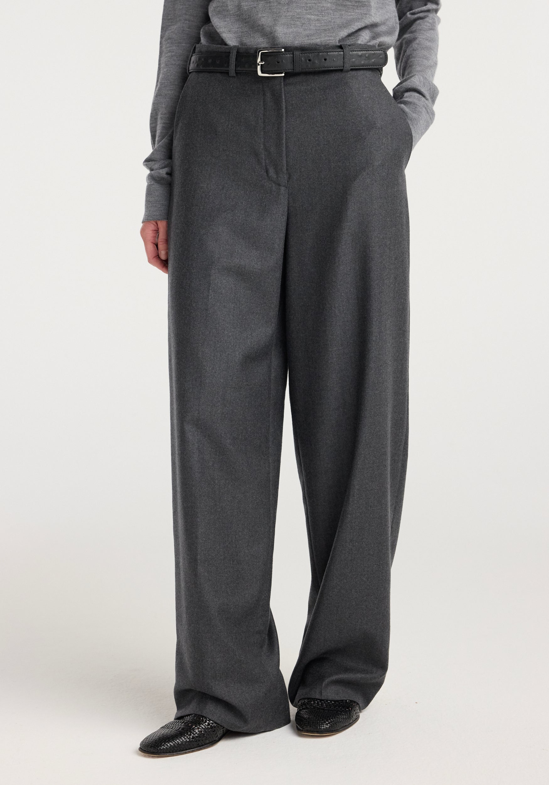 Model wearing wide leg trousers | dark grey melange paired with a grey top and black belt, styled with black textured shoes on a neutral background.