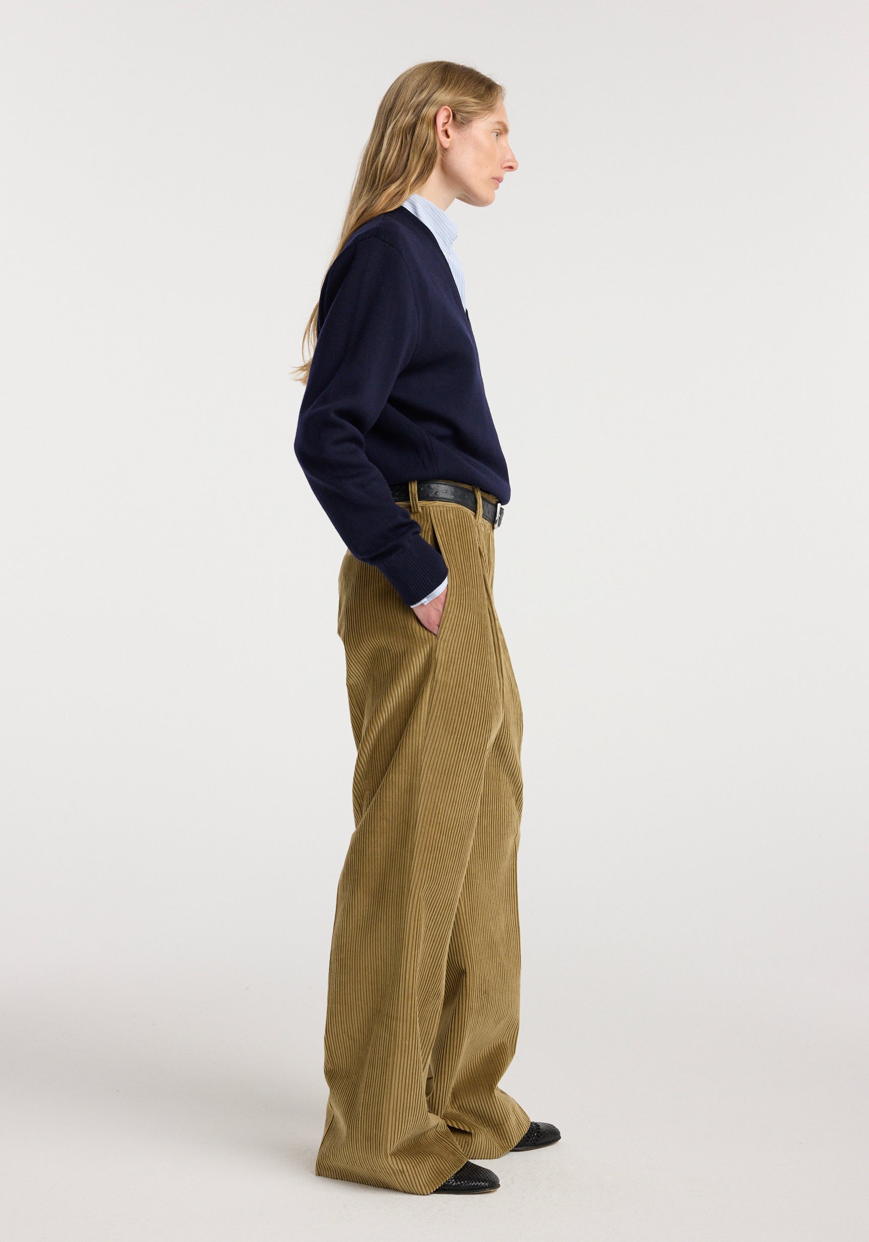Side view of a model wearing Ted - Lower waist corduroy trousers | beige, paired with a navy sweater and light blue shirt, showcasing the loose fit and textured fabric.