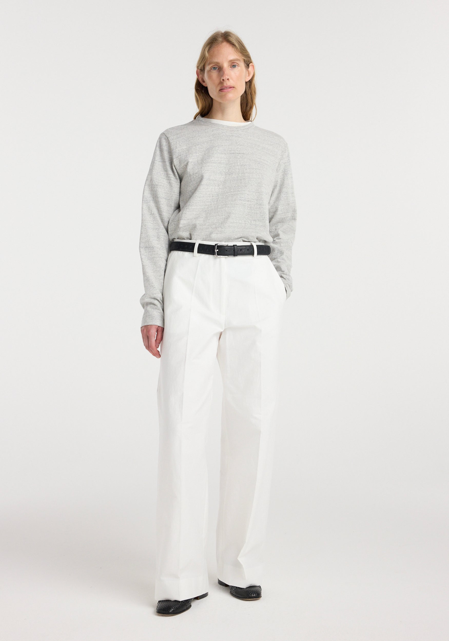 Woman wearing a grey long-sleeve top paired with Classic loose fit chino | optic white pants, styled with a black belt and black shoes against a plain white background.