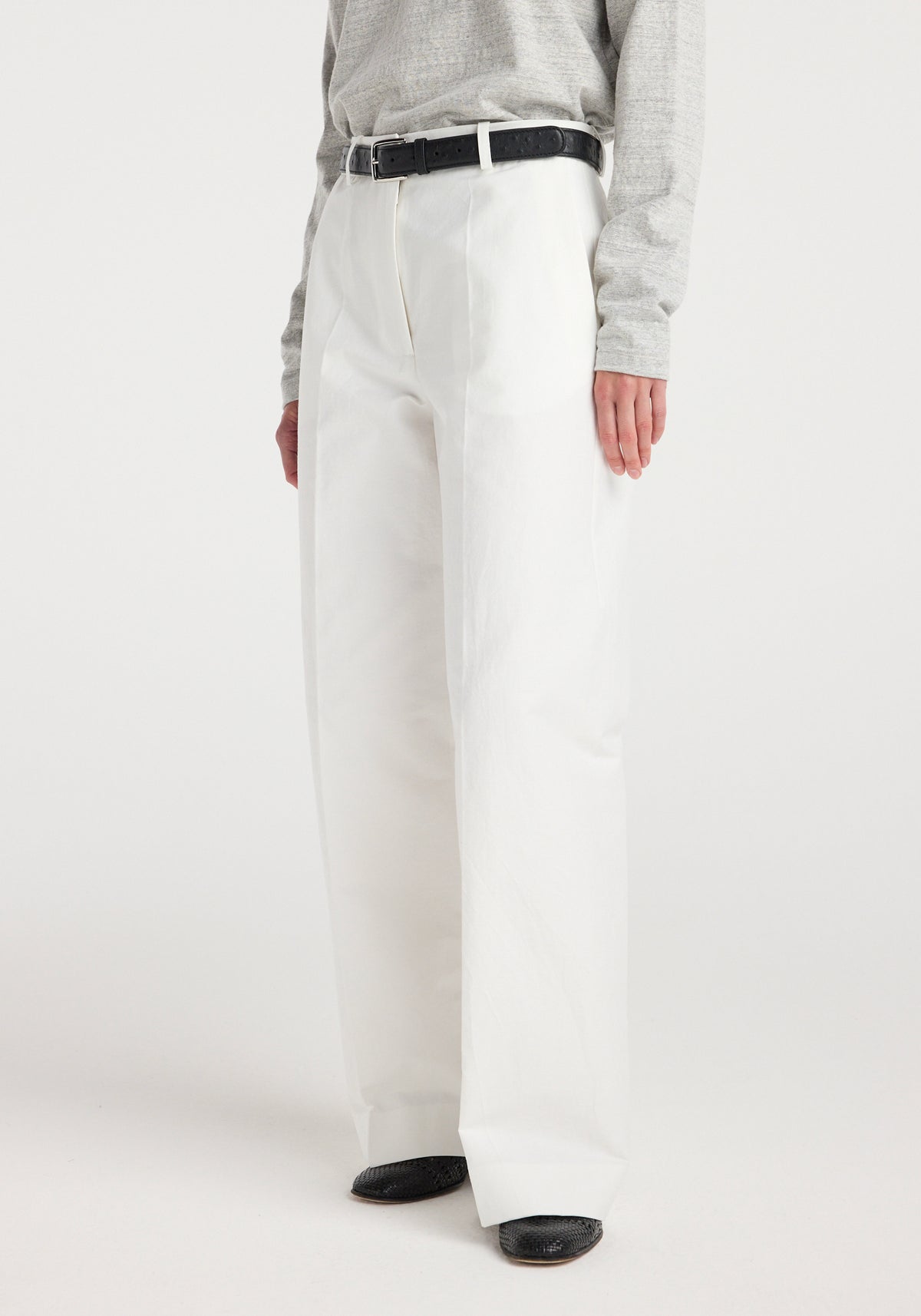 Model wearing Classic loose fit chino | optic white paired with a light grey long sleeve top, black belt, and black pointed shoes on a white background.