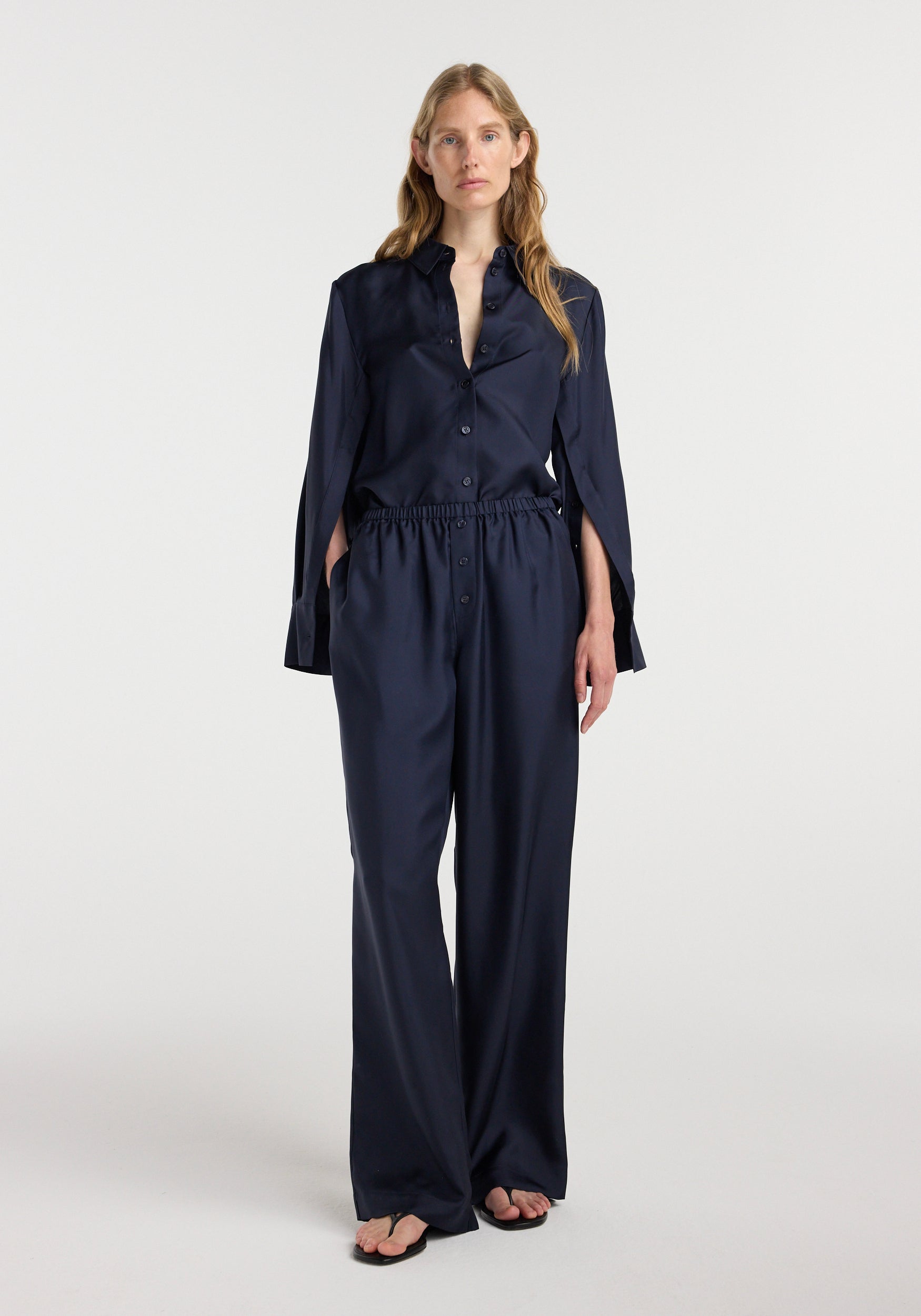 Front view of a woman wearing dark navy Silk relaxed trousers | night paired with a matching button-up silk shirt, standing against a plain white background.