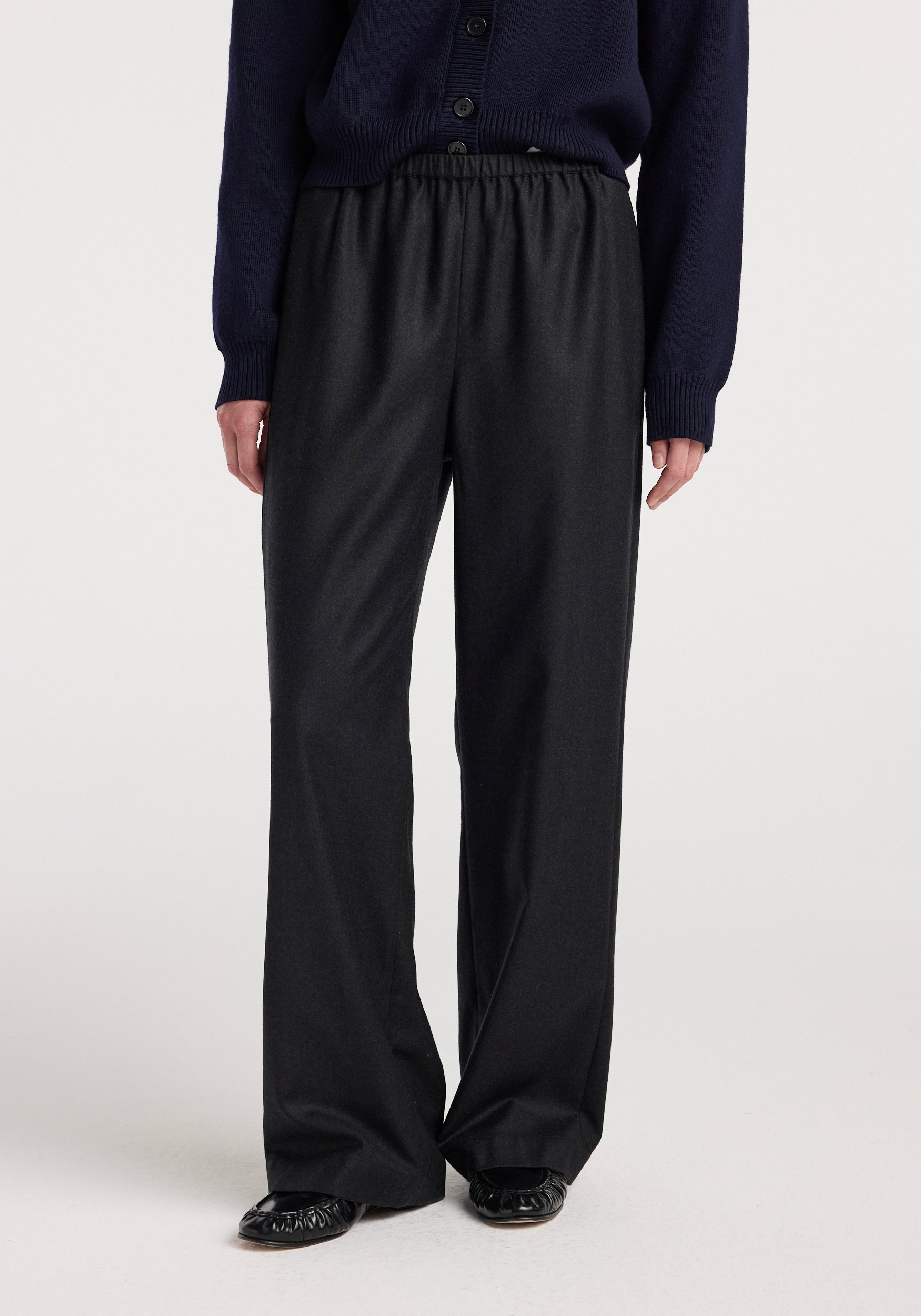 Front view of a person wearing relaxed fit trousers | anthracite melange with an elastic waistband, paired with a dark navy sweater and black shoes against a plain background.