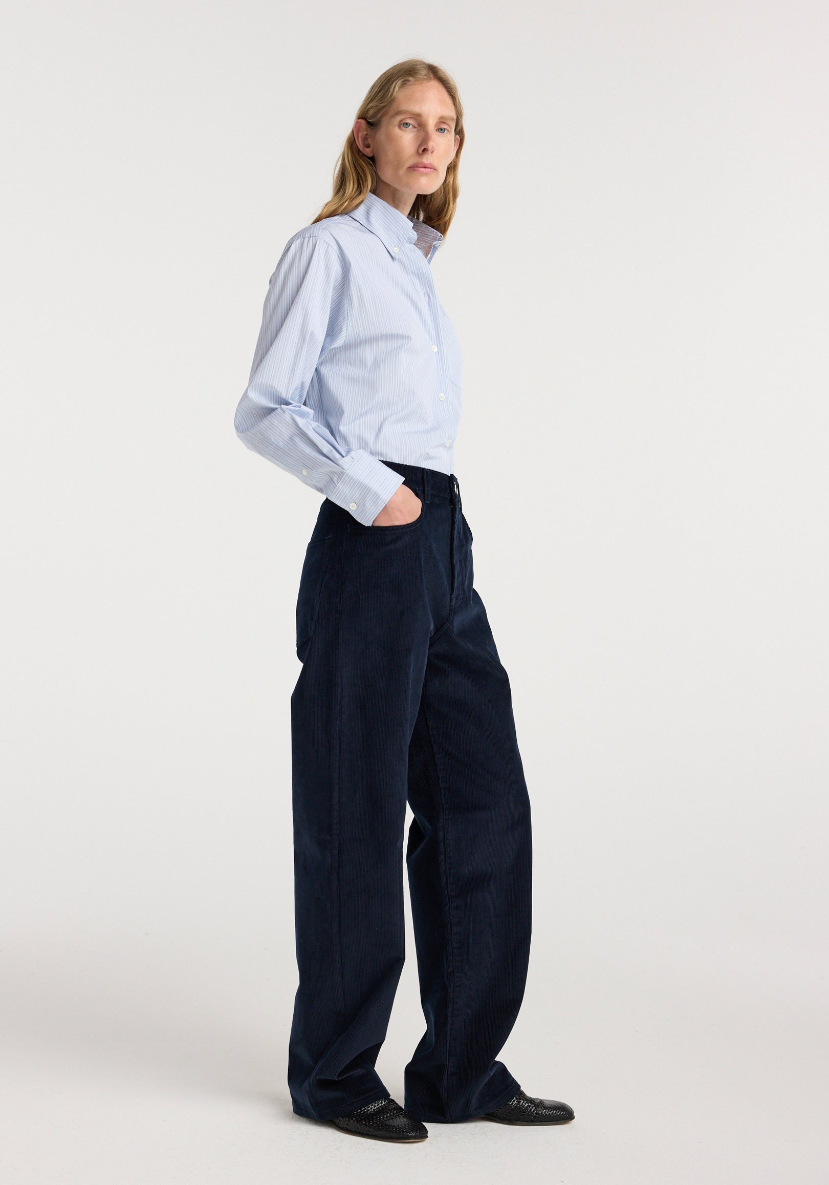 Model wearing Bruun - Signature baggy corduroy | night in dark navy corduroy, styled with a light blue button down shirt and black shoes in a studio setting