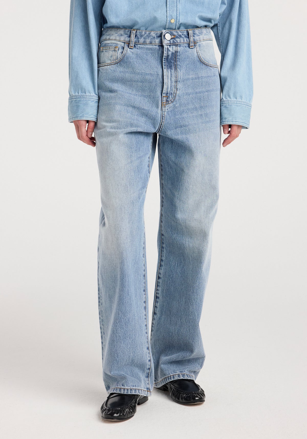 Front view of a person wearing Bruun - Signature baggy denim | classic blue paired with a light blue denim shirt and black shoes, highlighting the relaxed fit and faded classic blue wash.