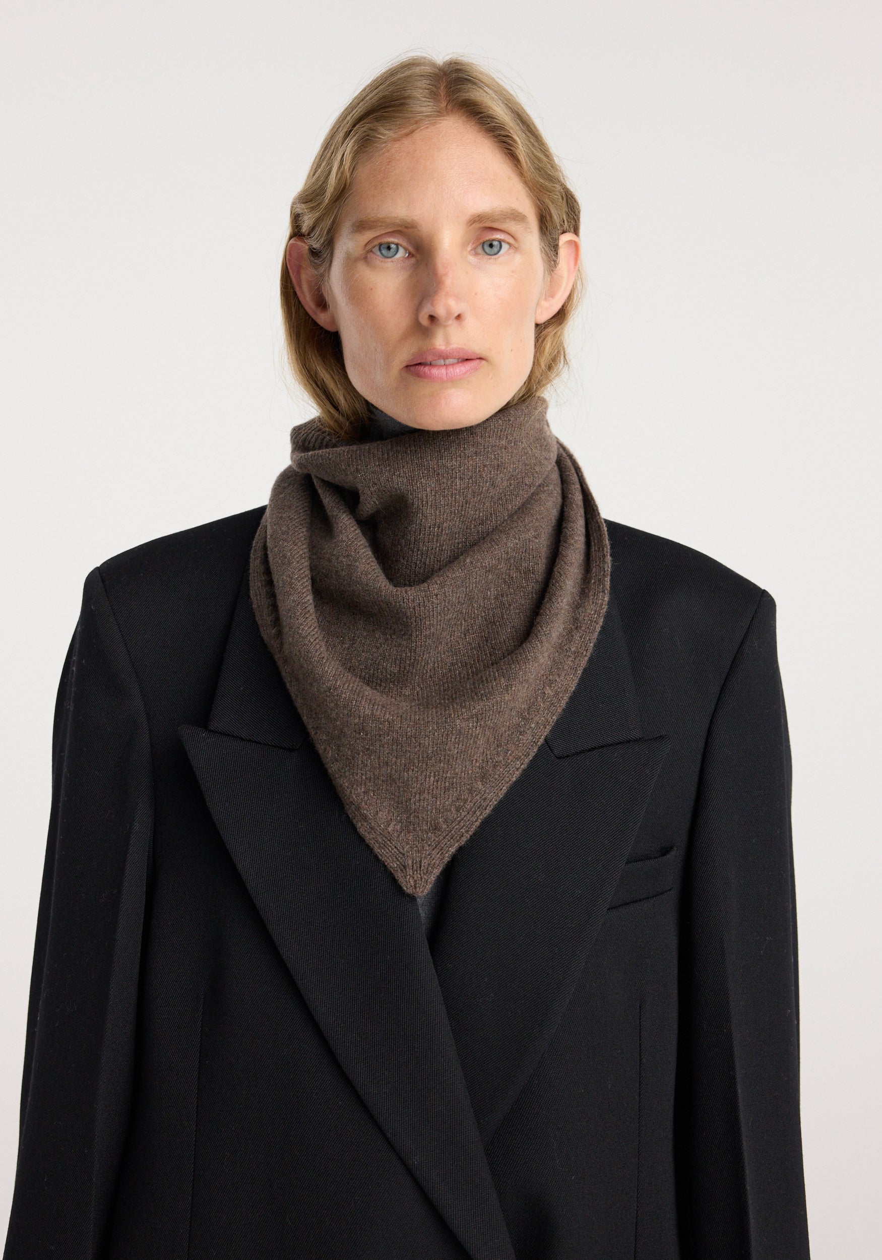 Model wearing a small knitted triangle scarf | brown melange styled over a black coat, showcasing the scarf’s cozy texture and rich brown melange color.