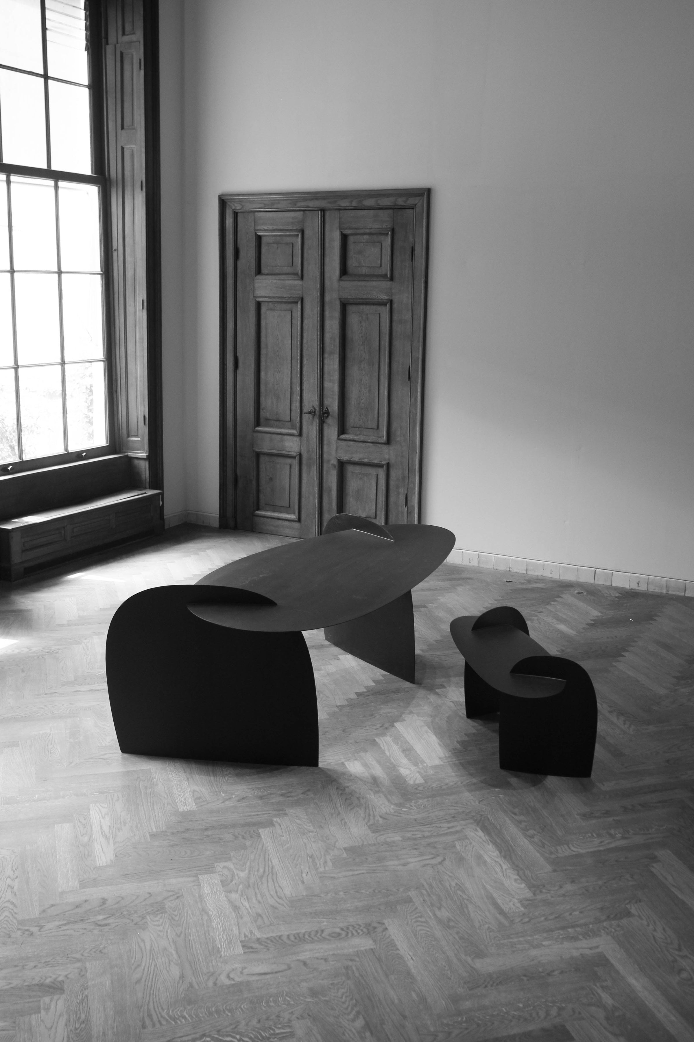Sculpted Table | 9845: Abstract oak wood table by Arne Kristian, featuring curved, interlocking black panels in a minimalist, well-lit room with herringbone floor.