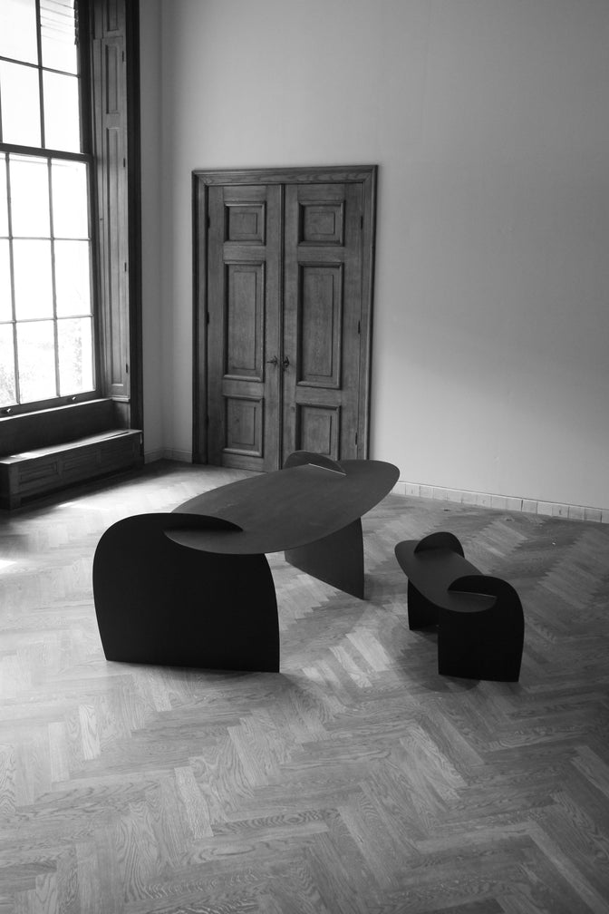 Sculpted Table | 9845: Abstract oak wood table by Arne Kristian, featuring curved, interlocking black panels in a minimalist, well-lit room with herringbone floor.