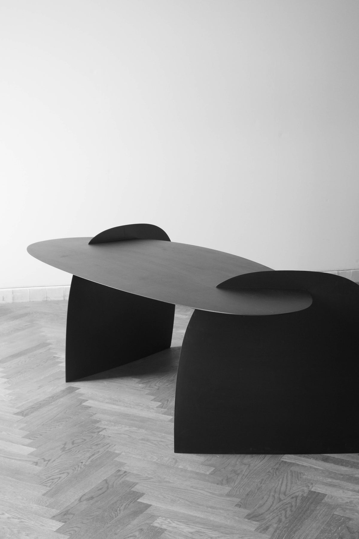 Sculpted Table | 9845: A minimalist, black, oak wood table by Arne Kristian, featuring an elongated oval top and semi-arched supports, displayed gallery-style.