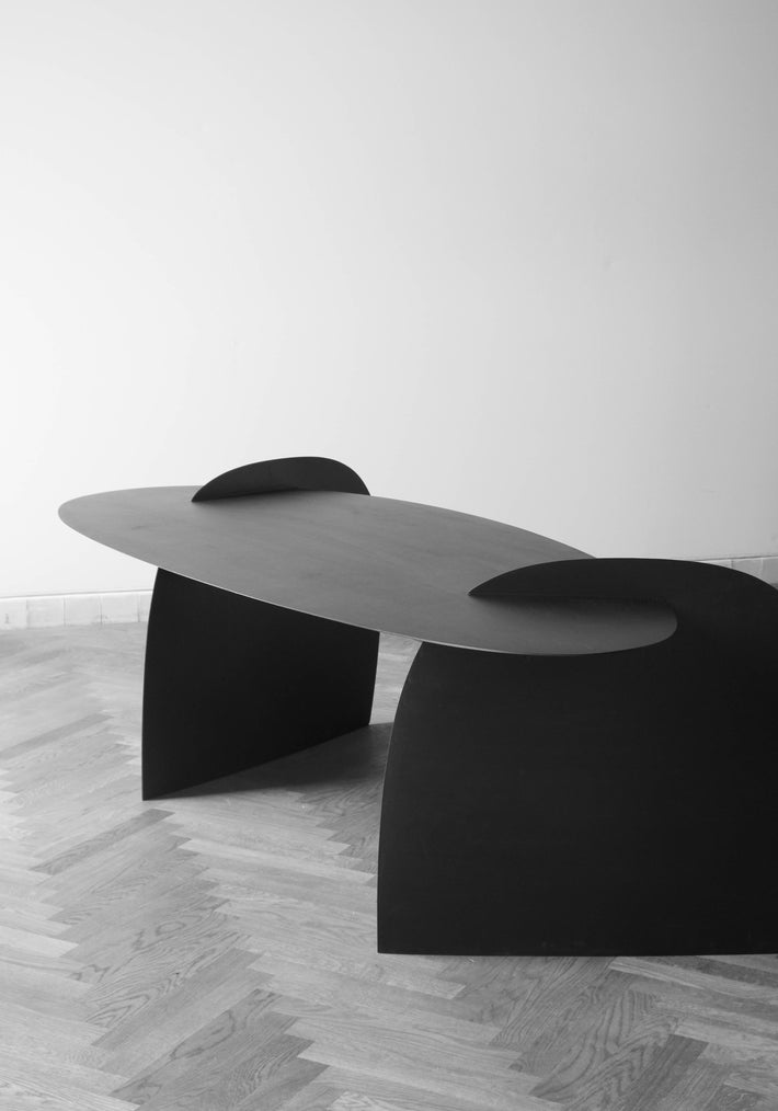 Sculpted Table | 9845: A minimalist, black, oak wood table by Arne Kristian, featuring an elongated oval top and semi-arched supports, displayed gallery-style.