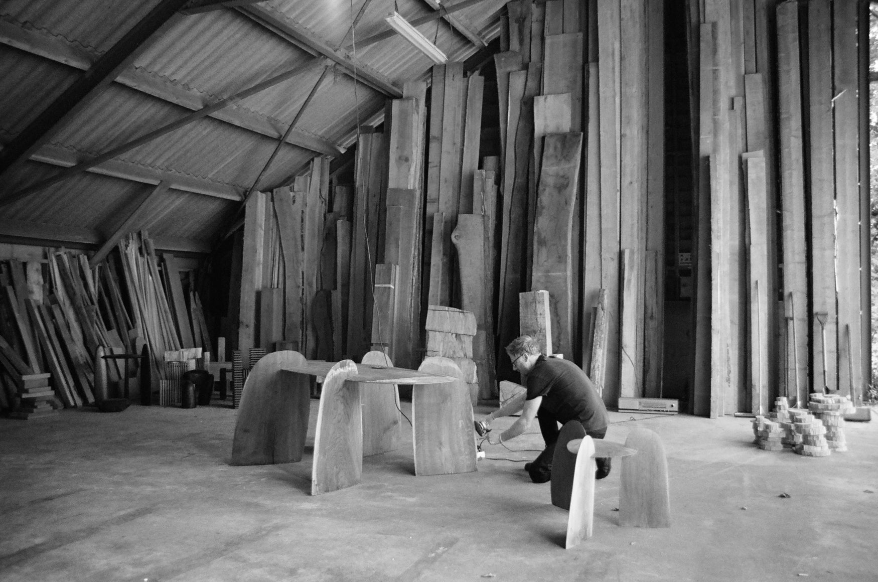 Person working with wooden furniture pieces in a workshop with wooden shelves leaning against all walls