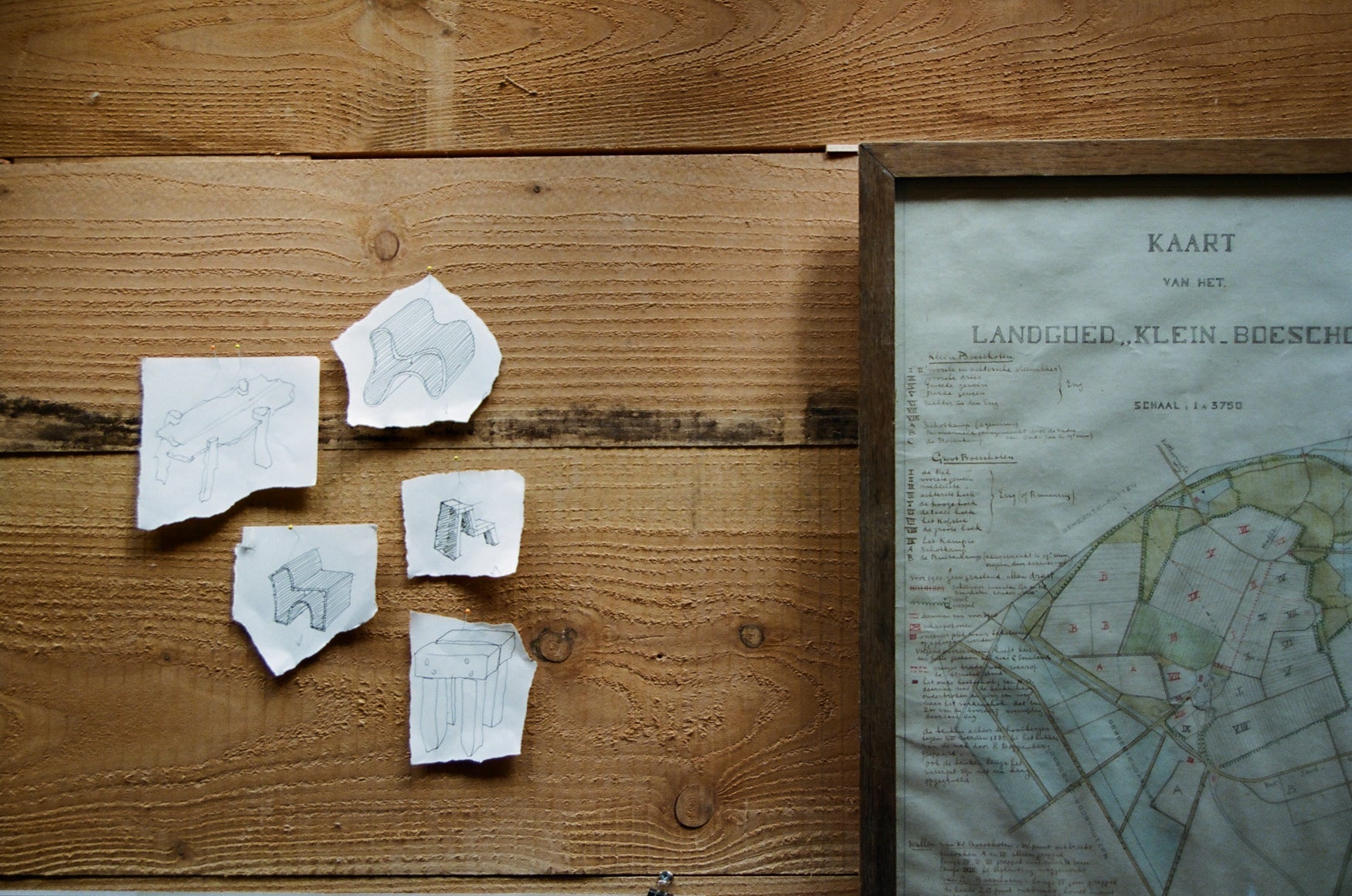 A wooden wall with small sketches of furniture pieces pinned against it and an old map of an estate