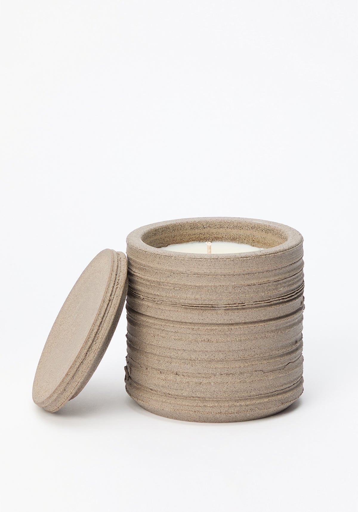 Diplomatico Scented Candle | stone in a textured, stone-colored ceramic container with a matching lid placed beside it, showing the unlit white wax inside.