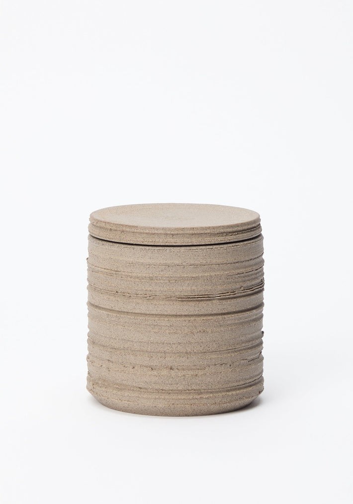 Diplomatico Scented Candle | stone: A sandy-colored cylindrical ceramic vessel with horizontal ridges, featuring a snug lid, handmade for lasting use and fragrance.