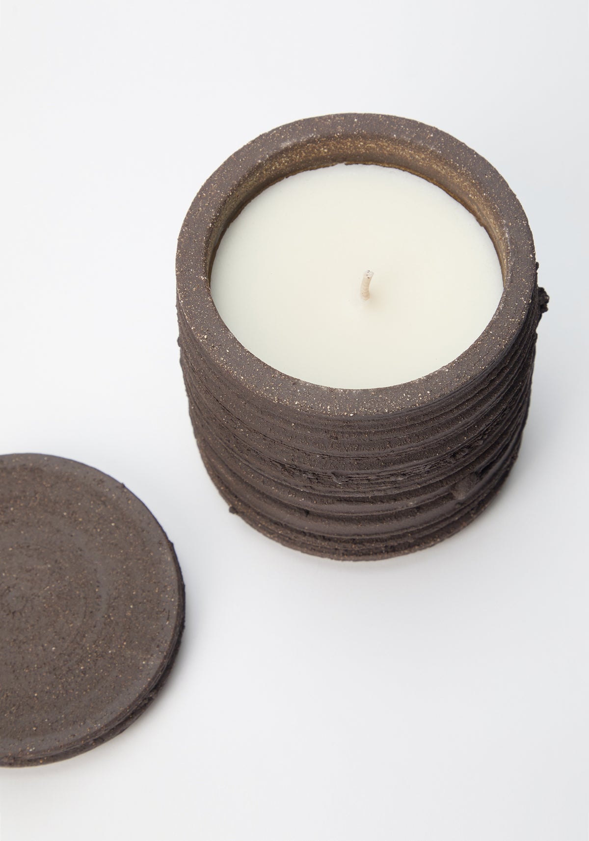 Open Diplomatico Scented Candle | soil showing the white wax inside a textured dark brown ceramic container with its matching lid placed beside it on a white surface.