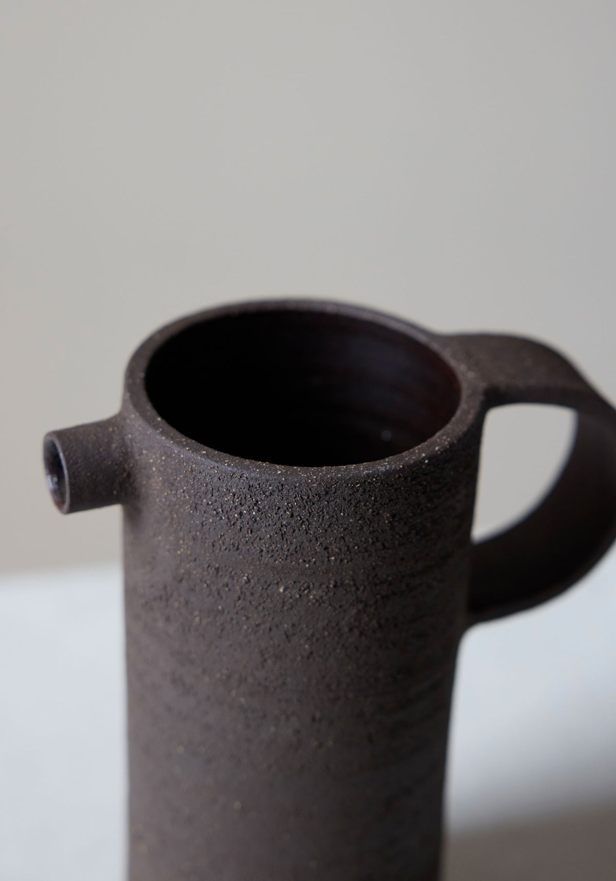 Close-up of a dark textured ceramic carafe with a small spout and handle, showcasing the rustic surface of the Ceramic Carafe | soil.