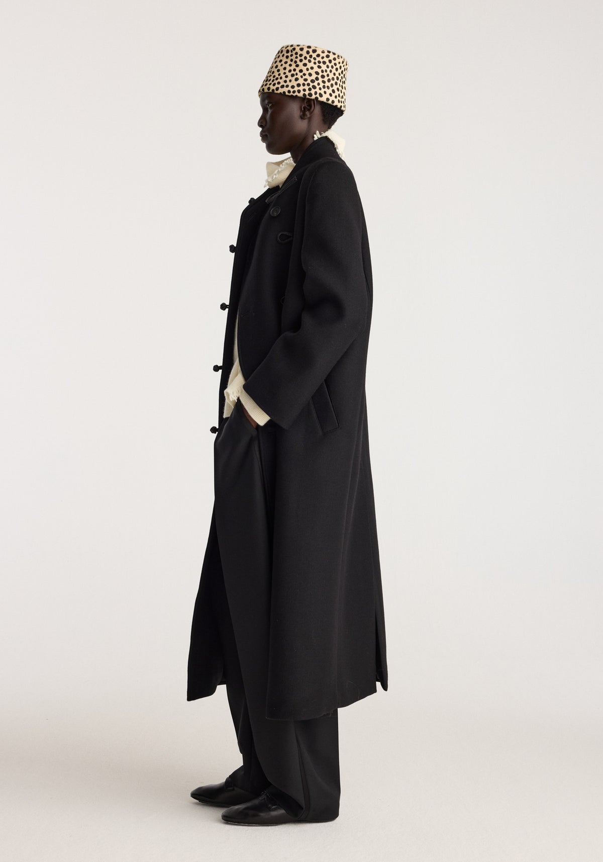 Cheetah leather hat | cheetah worn in profile with a spotted pattern, styled with a long black coat and dark trousers for a sleek fashion look