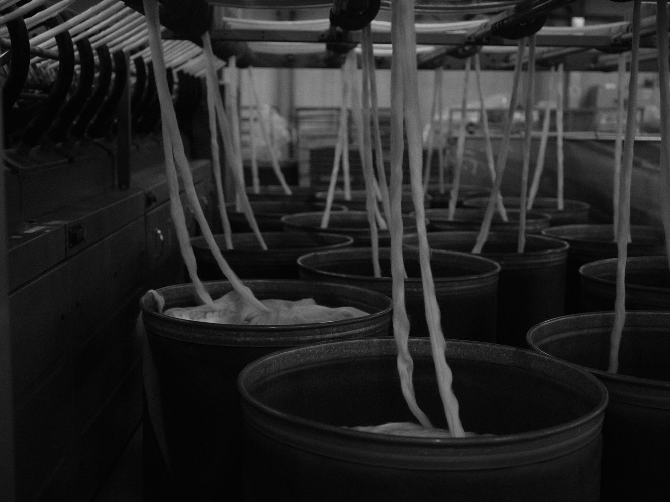 Black and white image of threads of white wool yarns dropping down in big bins with a blurred background