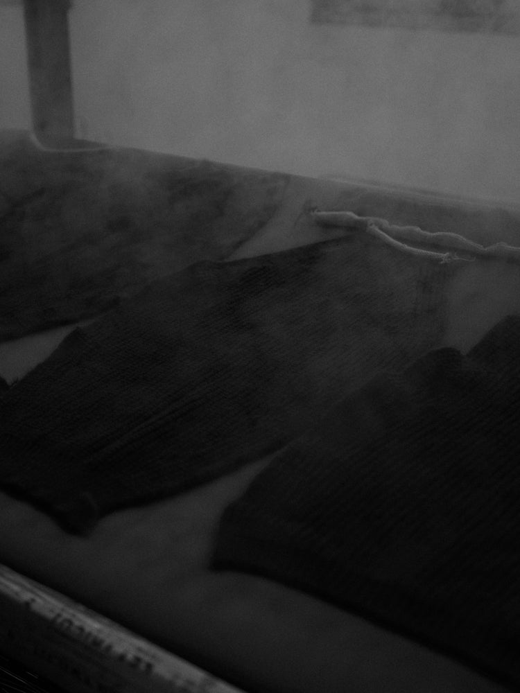 Pieces of a knitted sweater laying flat on a steaming board with steam coming off 