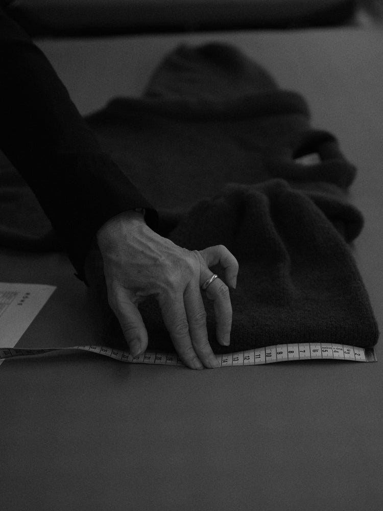 Close-up of someone's hand measuring a knitted sweater with a measuring tape on a table