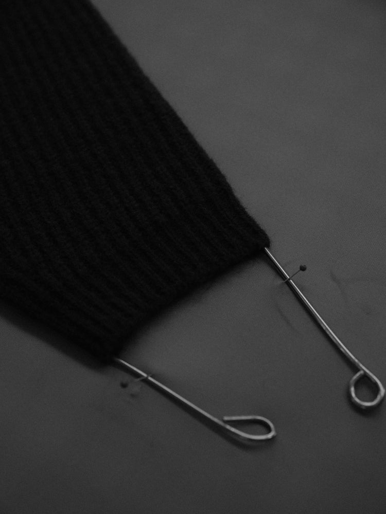 Close-up of a sleeve of a knitted sweater pinned on a steaming table with metal rods