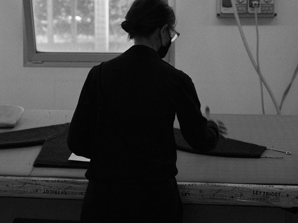 Woman working behind a steaming table with a knitted sweater pinned to it 
