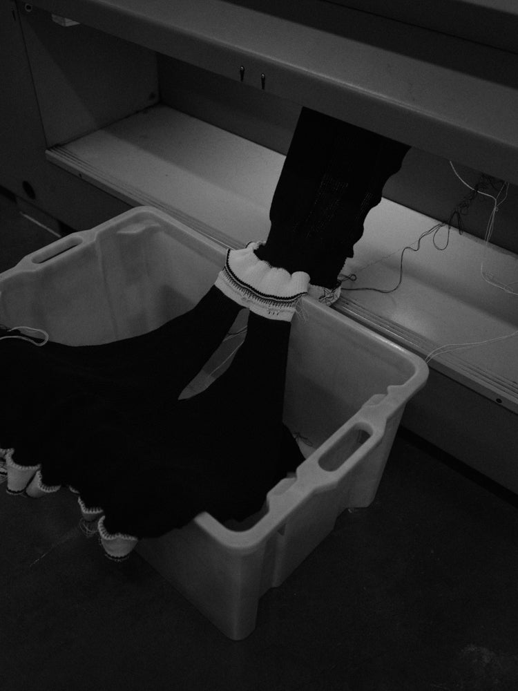 Pieces of a v-neck sweater coming out of a knitting machine