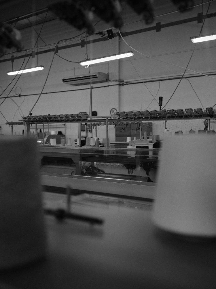 Black and white interior of a knitted factory with spools of yarn and tl lights
