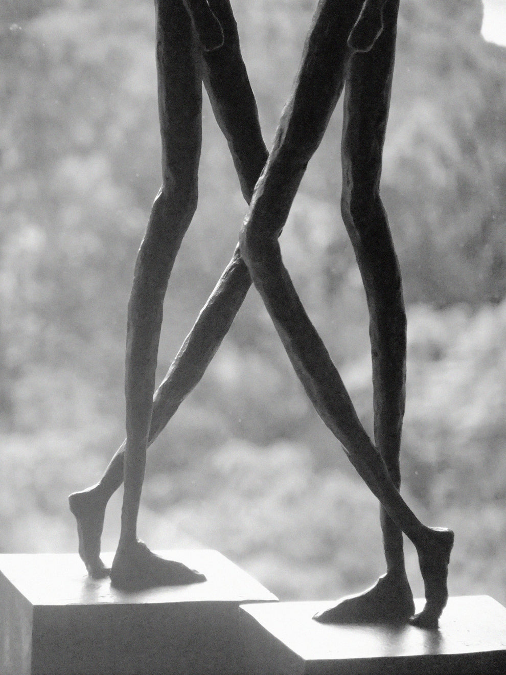 Legs of two elegant slim bronze figures against a blurred leafy background
