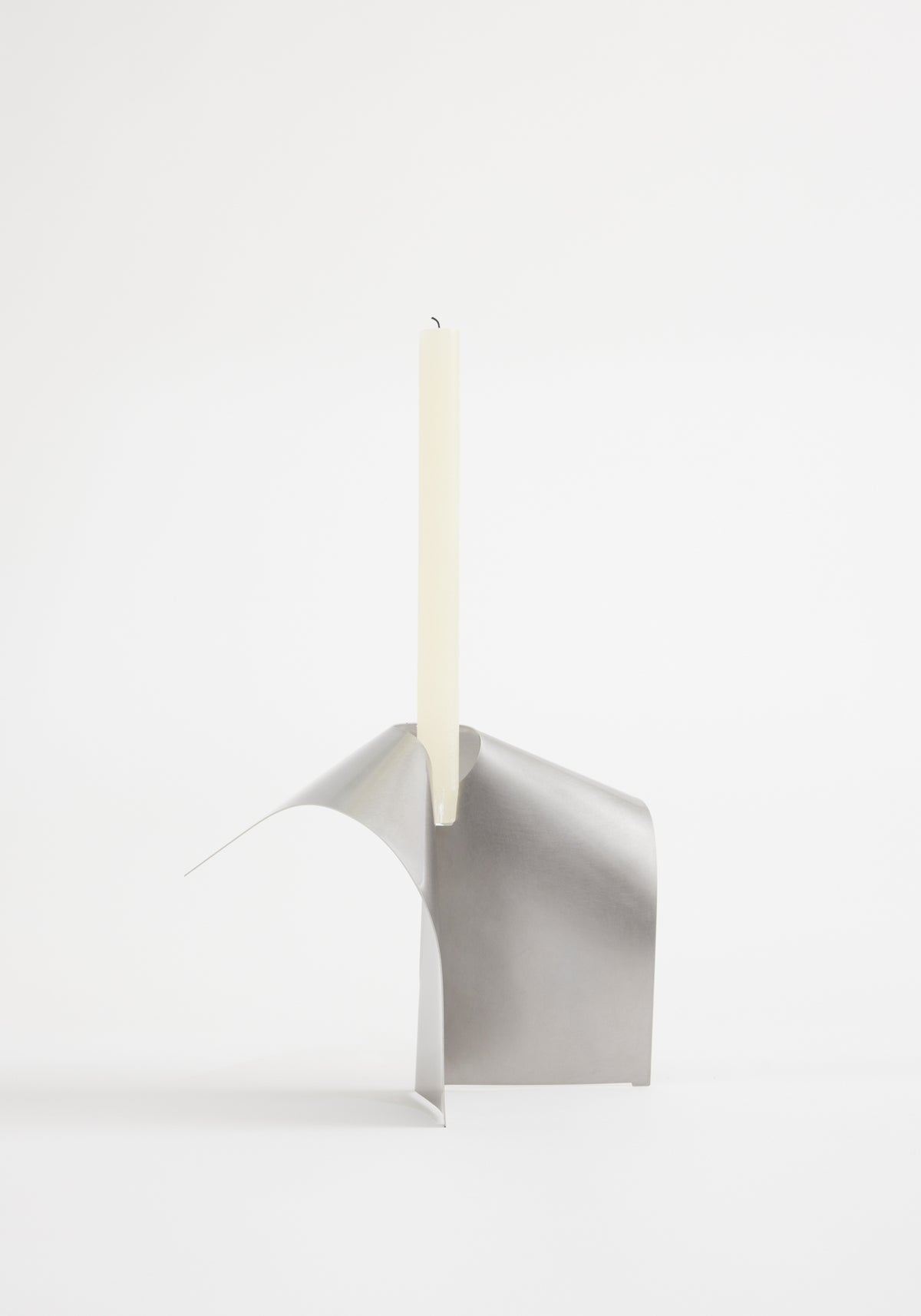 Minimalist modern Stainless steel candle holder | Stainless steel with a sleek curved design holding a tall, unlit white taper candle against a plain white background.