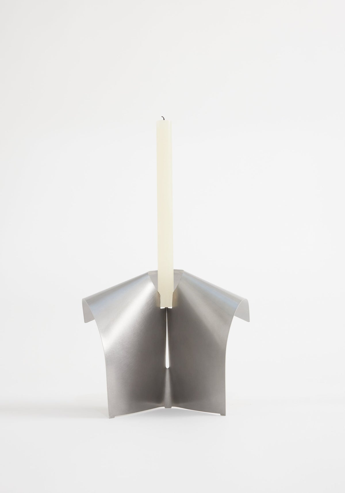 Stainless steel candle holder with three folded metal petals, holding an ivory taper candle, showcasing minimalist design by Dutch designer Paul Coenen.