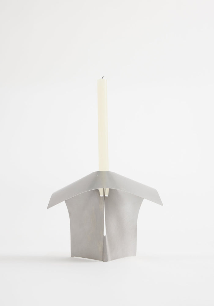 Stainless steel candle holder showcasing a minimalist, bent design with a slender white taper candle, handcrafted from stainless steel in collaboration with designer Paul Coenen.