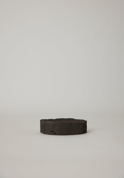 Round Tray handcrafted from lava stone, featuring a carved indent, shown with wooden sticks on a marble windowsill. Unique and available on request.
