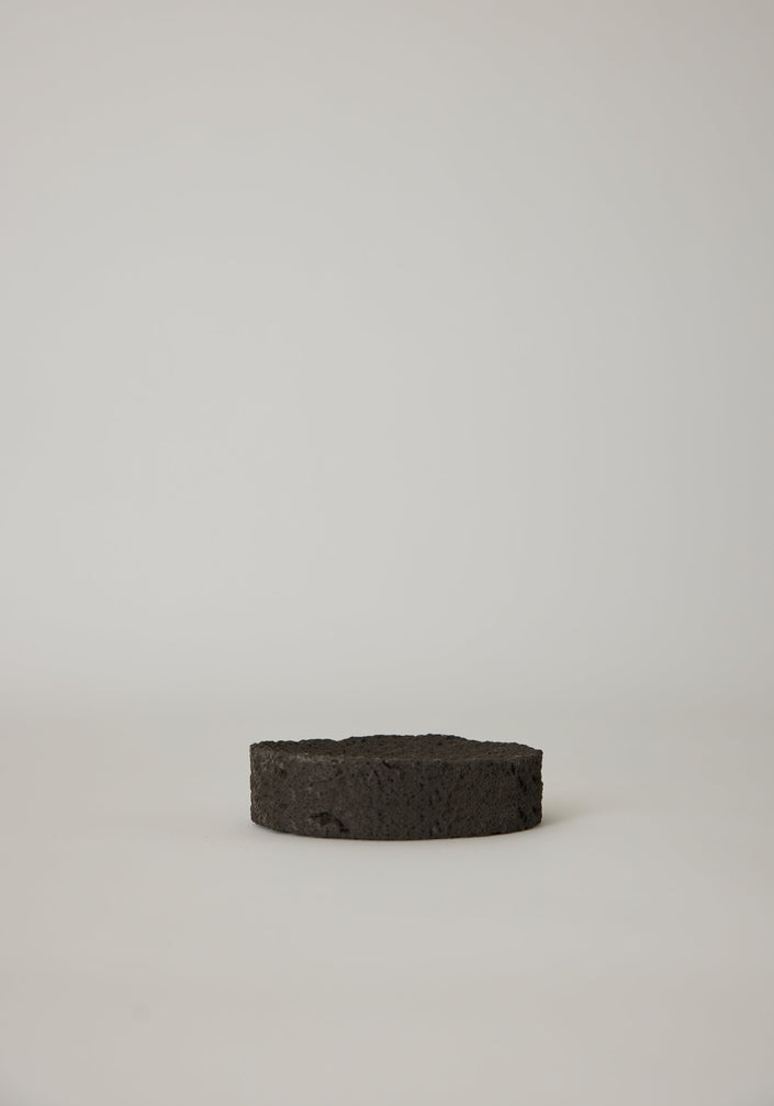 Round Tray handcrafted from lava stone, featuring a carved indent, shown with wooden sticks on a marble windowsill. Unique and available on request.