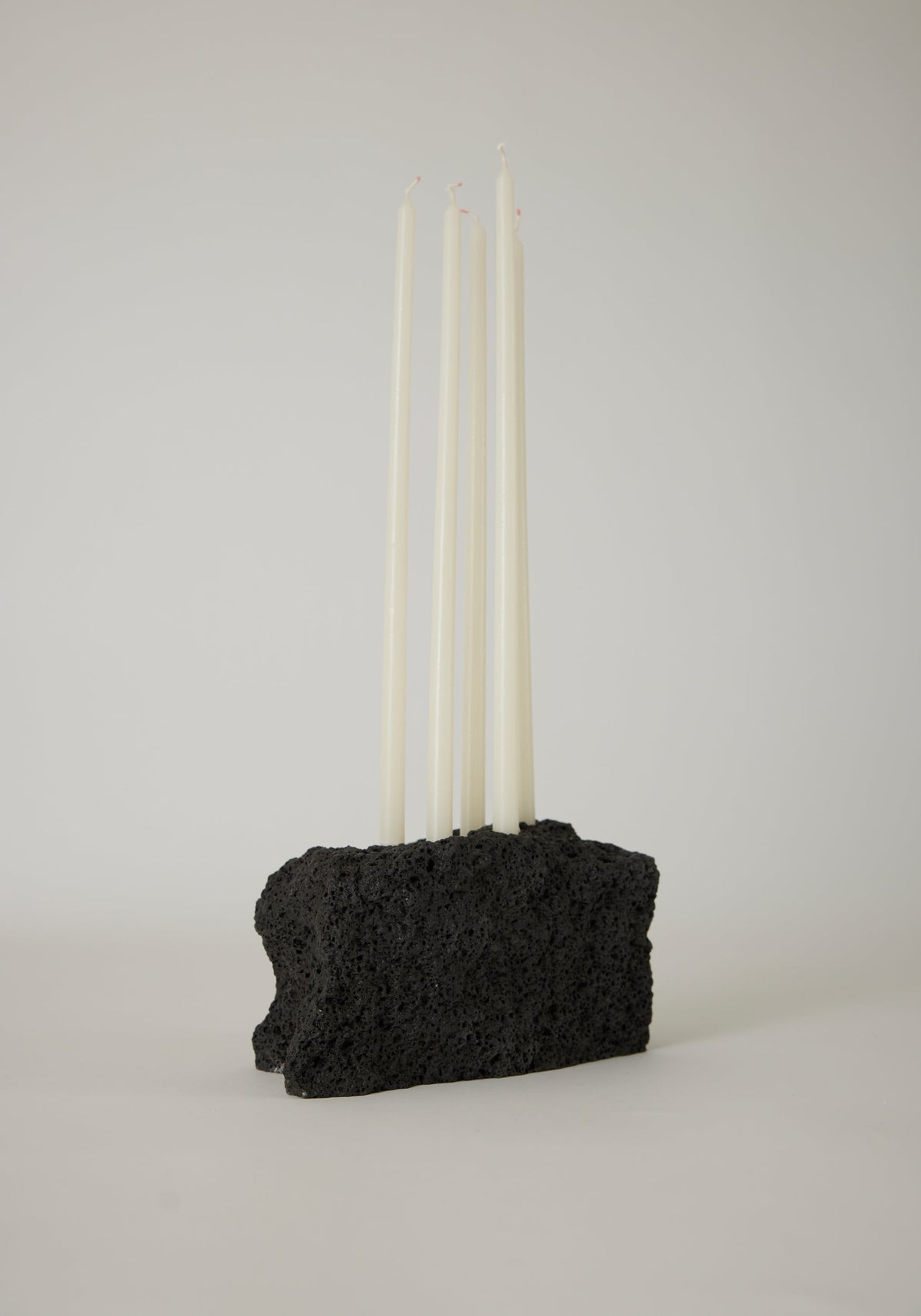 Sculptural Stone Candle Holder features six unlit white taper candles set in a handcrafted black porous lava stone block, measuring 10 cm high.