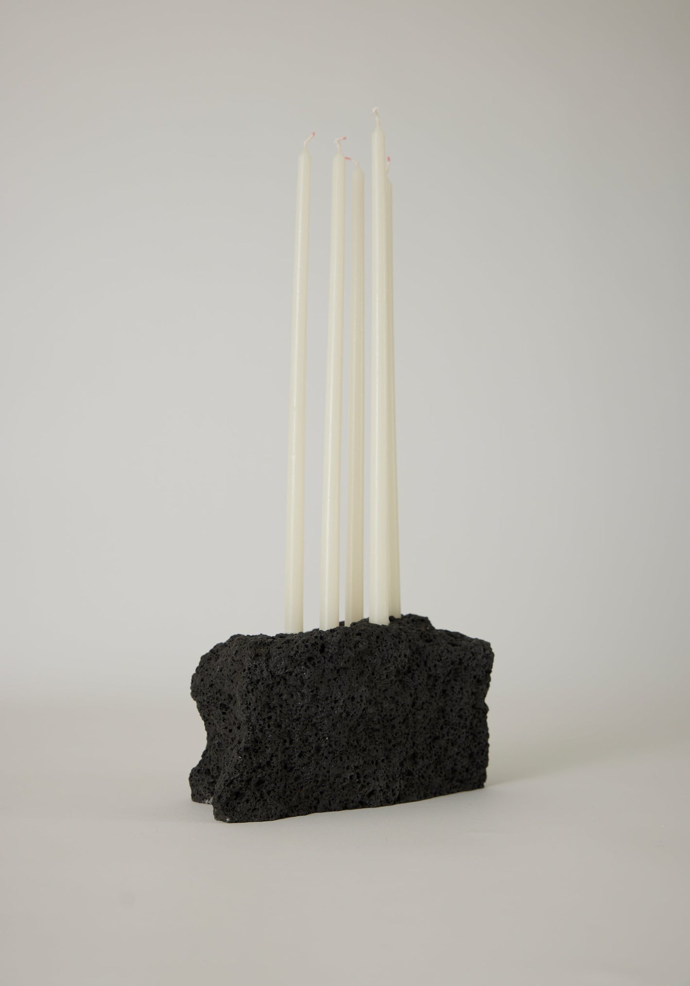 Sculptural Stone Candle Holder features six unlit white taper candles set in a handcrafted black porous lava stone block, measuring 10 cm high.