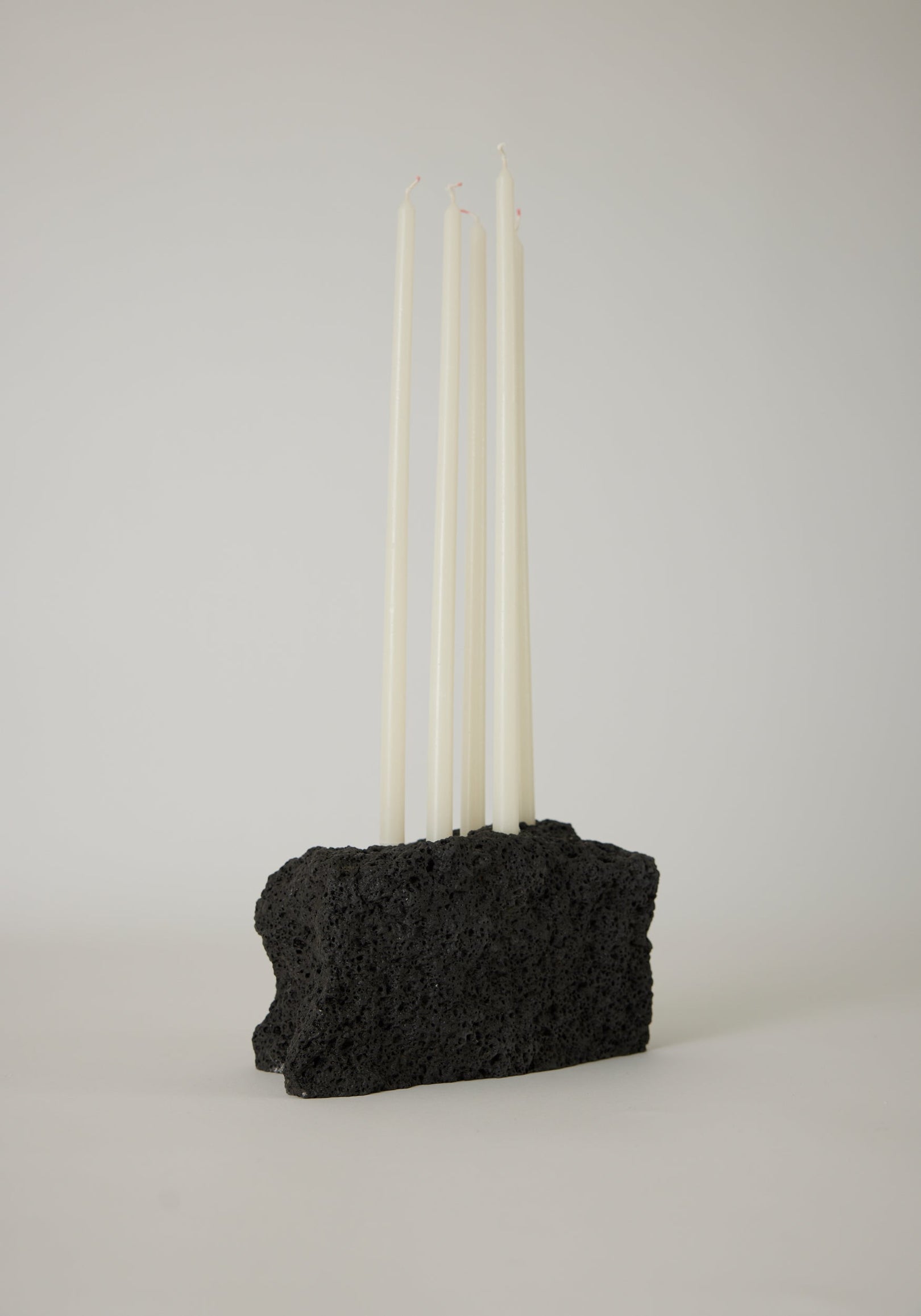 Sculptural Stone Candle Holder features six unlit white taper candles set in a handcrafted black porous lava stone block, measuring 10 cm high.