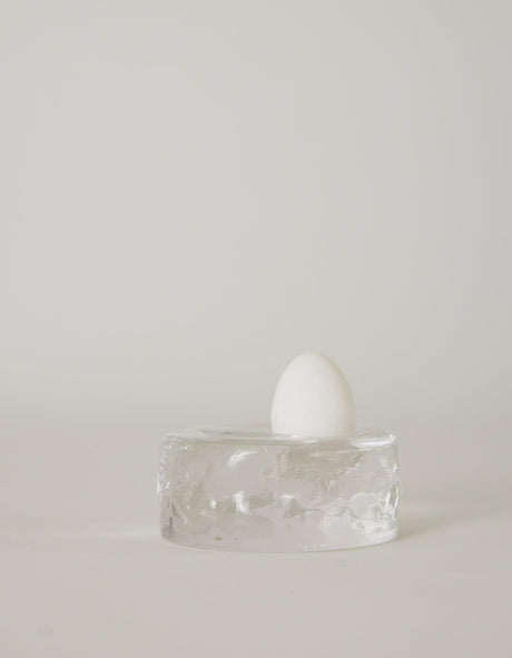 Presse-papier & holder | Glass: A single white egg stands on a transparent glass block, showcasing Szkło Studio's unique hand-blown craftsmanship and experimental design.