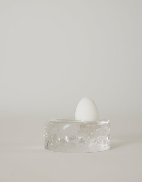 Presse-papier & holder | Glass: A single white egg stands on a transparent glass block, showcasing Szkło Studio's unique hand-blown craftsmanship and experimental design.