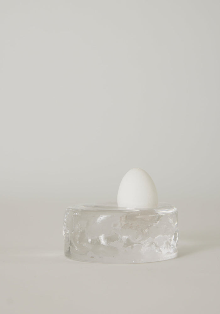 Presse-papier & holder | Glass: A single white egg stands on a transparent glass block, showcasing Szkło Studio's unique hand-blown craftsmanship and experimental design.