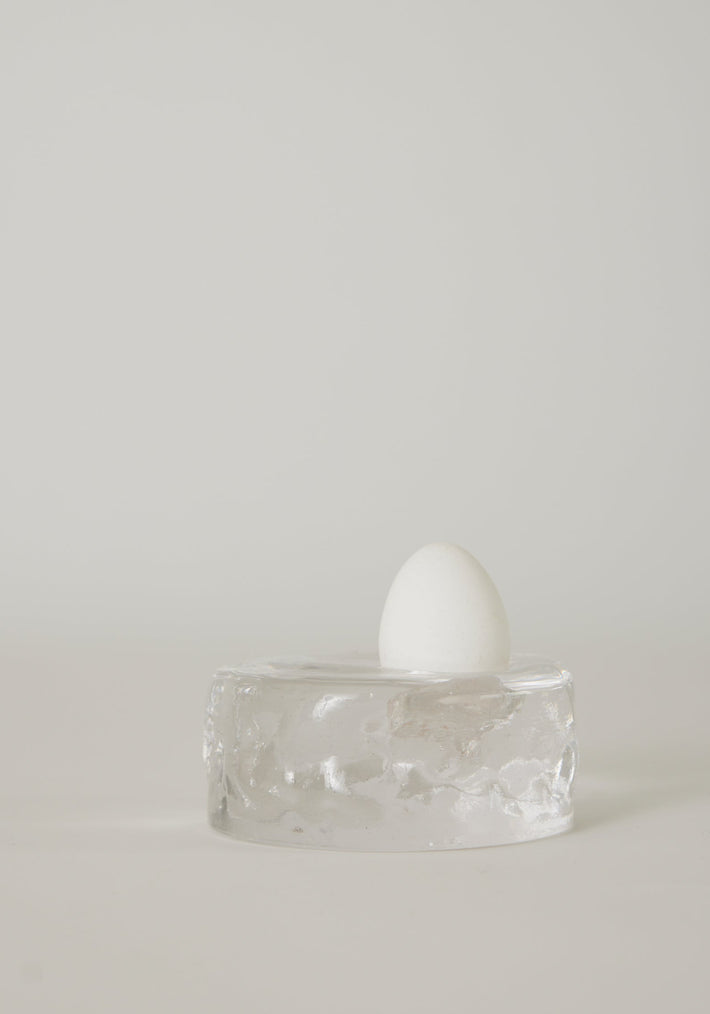 Presse-papier & holder | Glass: A single white egg stands on a transparent glass block, showcasing Szkło Studio's unique hand-blown craftsmanship and experimental design.