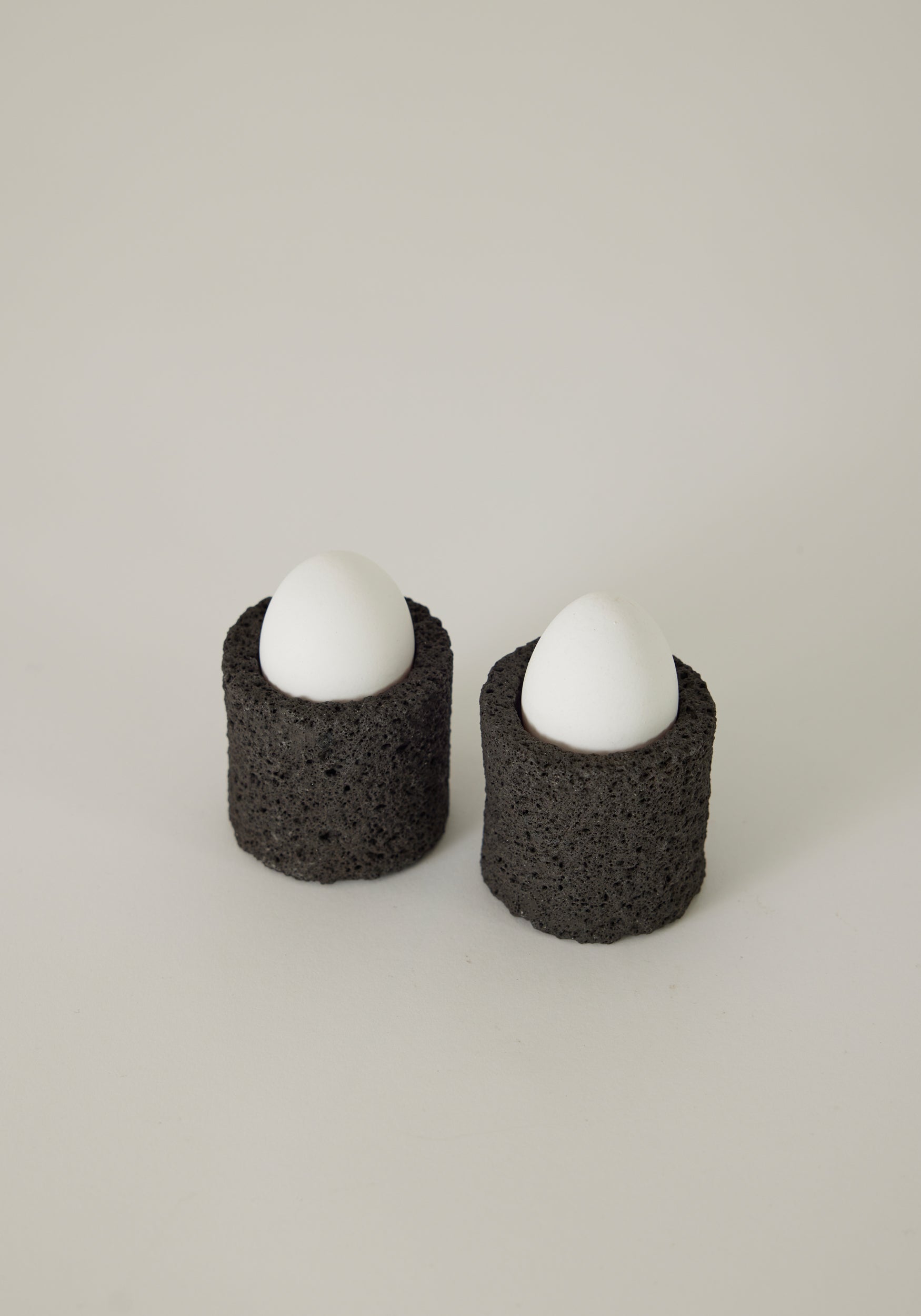 Two lava stone egg cups with white eggs inside on a white background