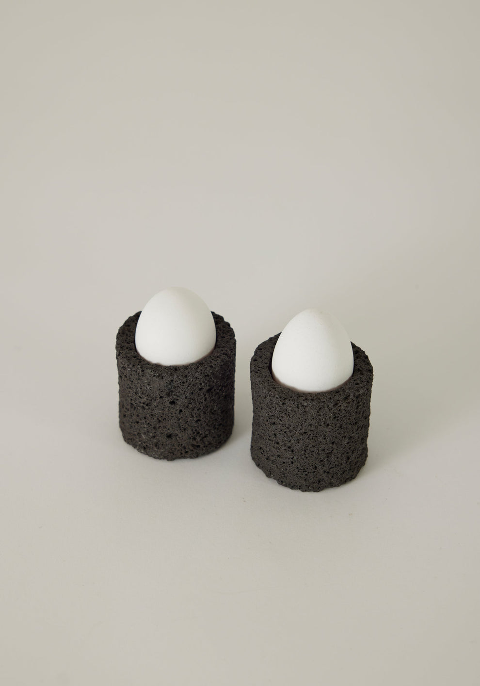 Two lava stone egg cups with white eggs inside on a white background