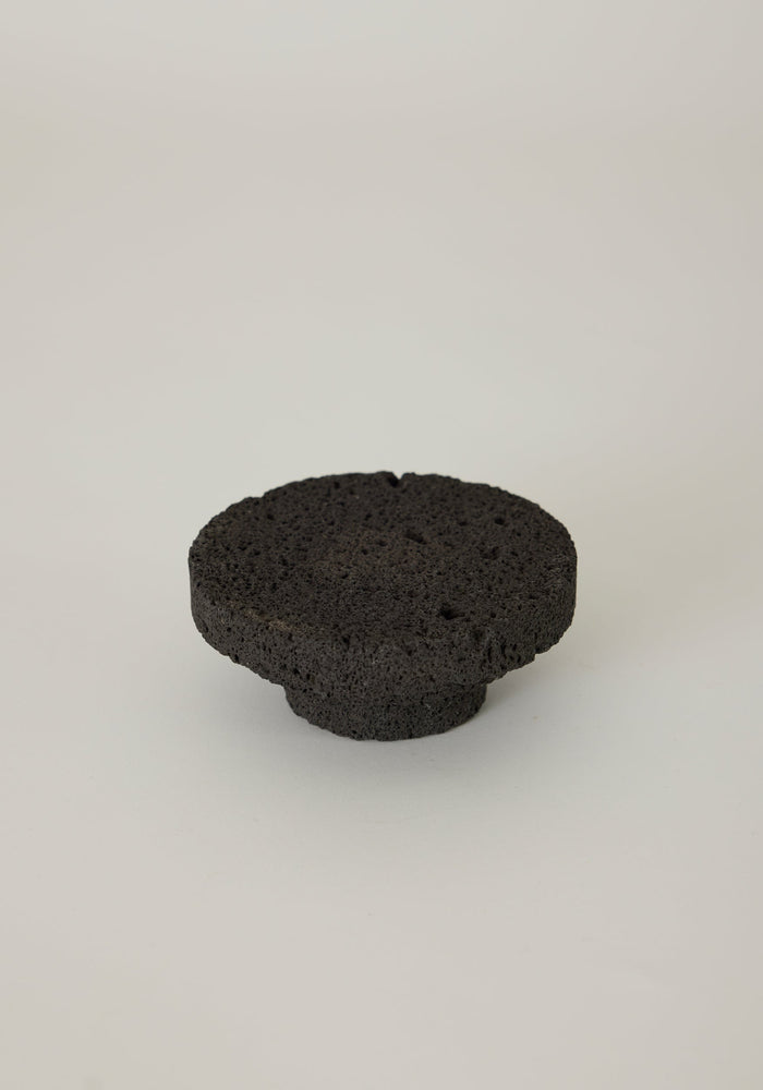 Elevated Sculptural Tray, a handcrafted disc-shaped tray made of porous lava stone by Louis Crombag, showcasing unique gas-bubble holes on a rounded base.