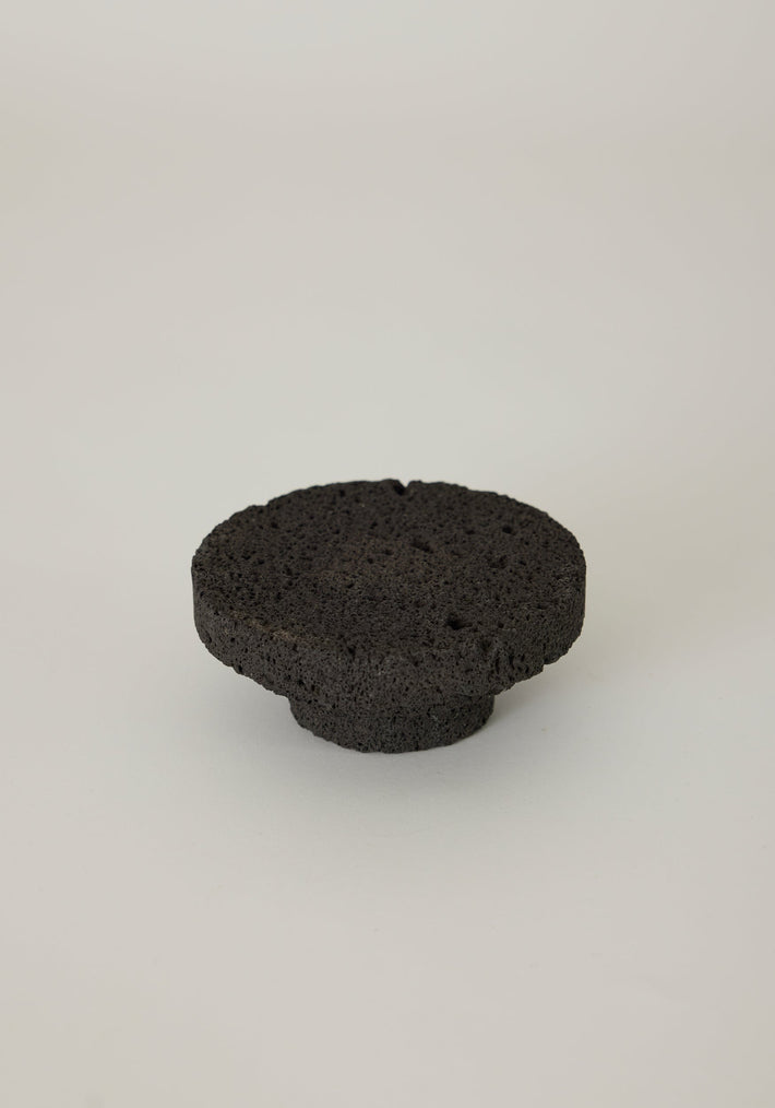 Elevated Sculptural Tray, a handcrafted disc-shaped tray made of porous lava stone by Louis Crombag, showcasing unique gas-bubble holes on a rounded base.