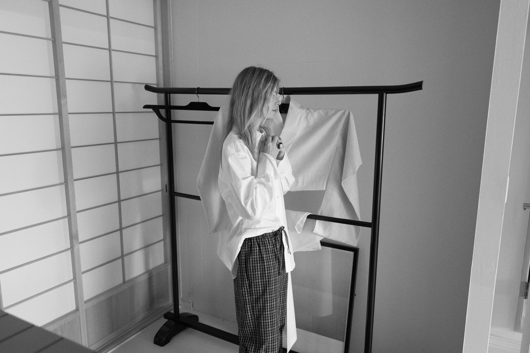 woman buttoning a white shirt standing in a Japanese interior