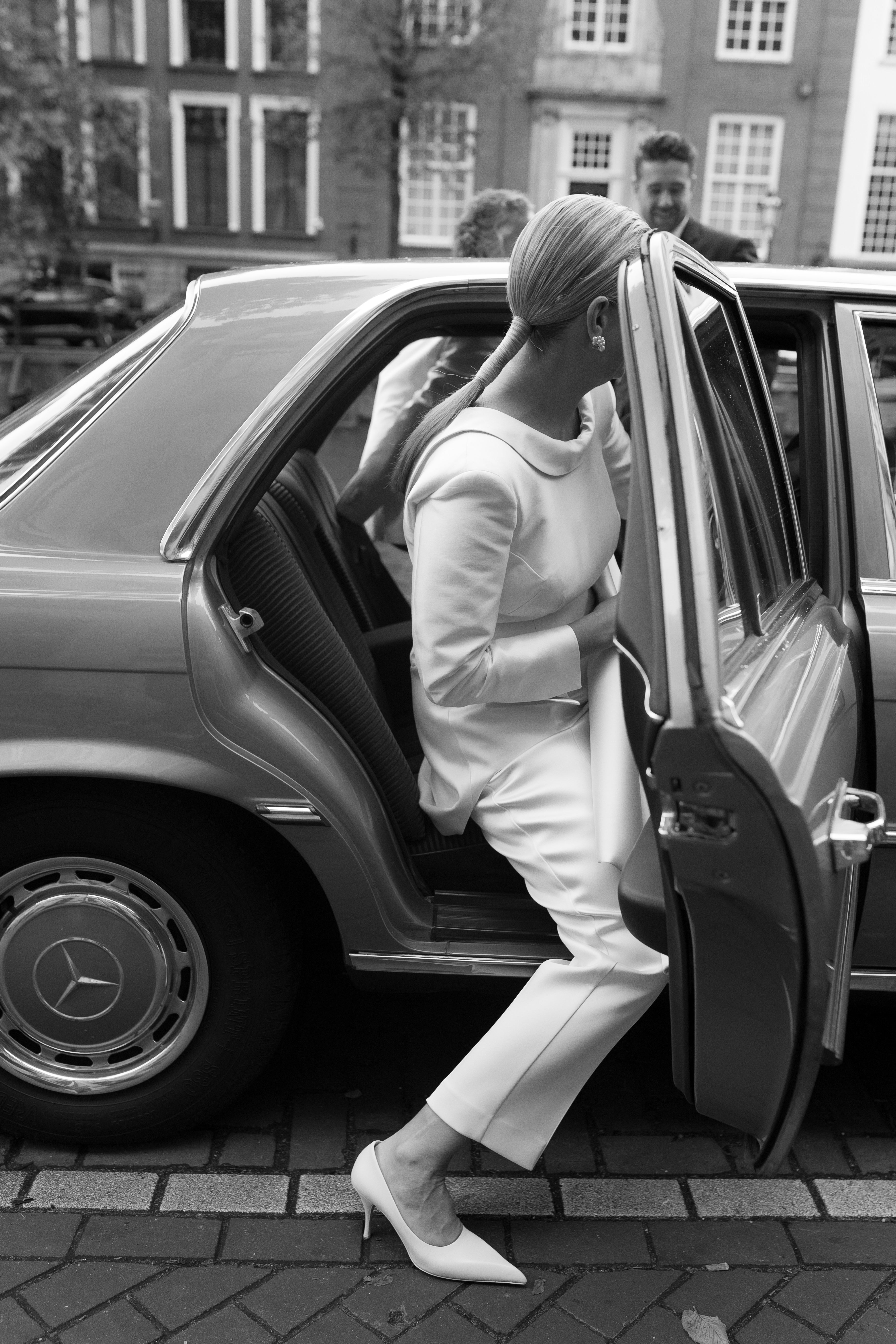 Woman wearing a white suit getting into a car. 