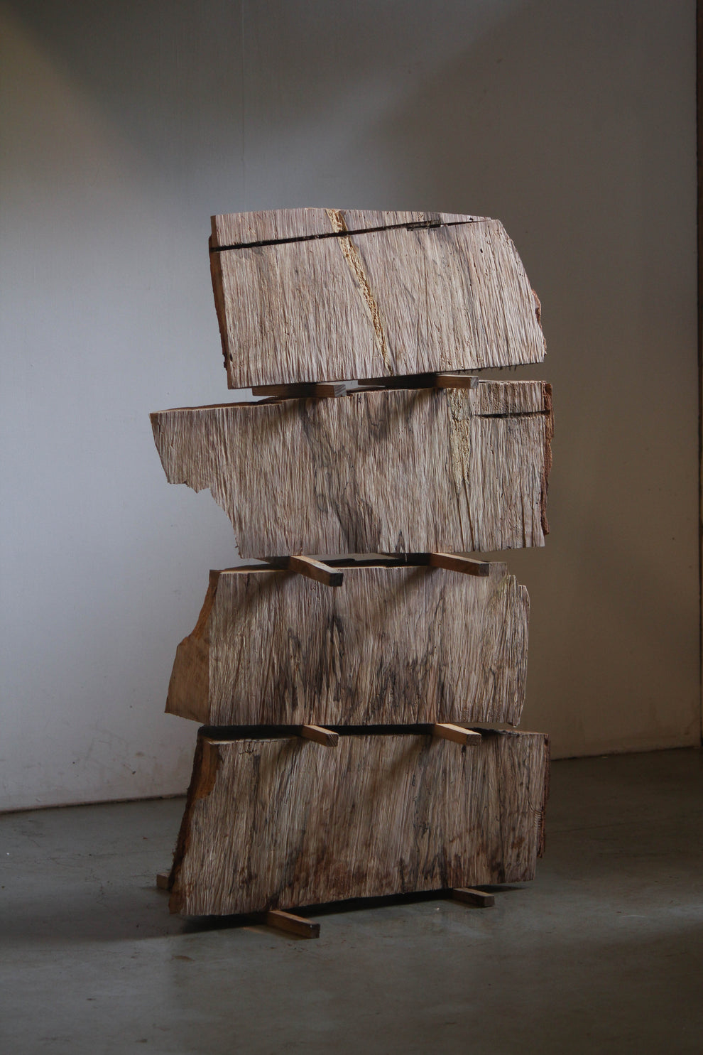 Wooden blocks stacked on top of eachother on a concrete floor against a white wall