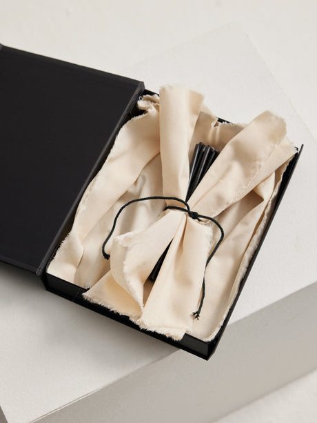 Candles 5mm | noir: A black box with a tied white-cotton cloth revealing a bundle of 30 slender, 10 cm tall beeswax candles.